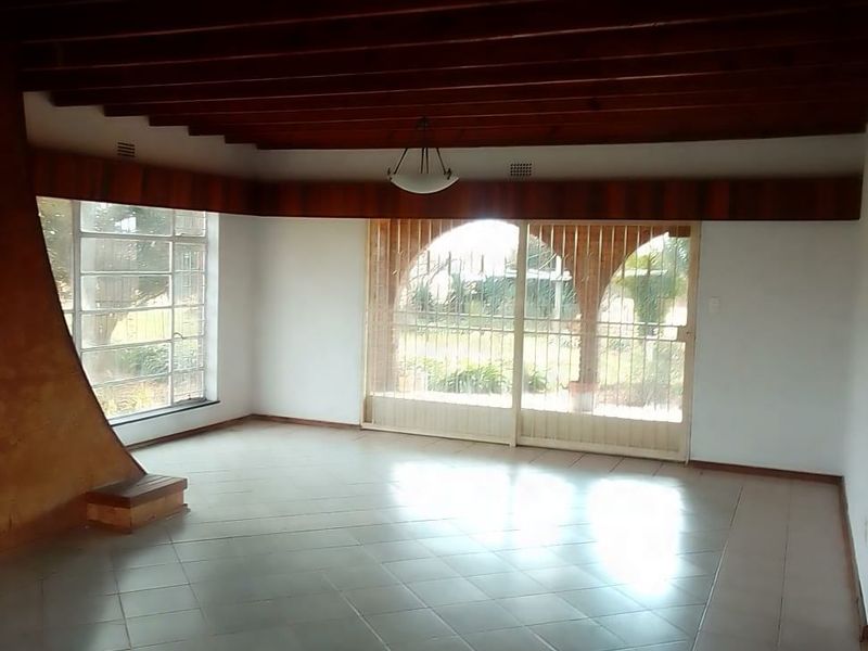 Spacious living area featuring exposed timber beam ceilings, tiled flooring, and large sliding doors providing access to the garden.
