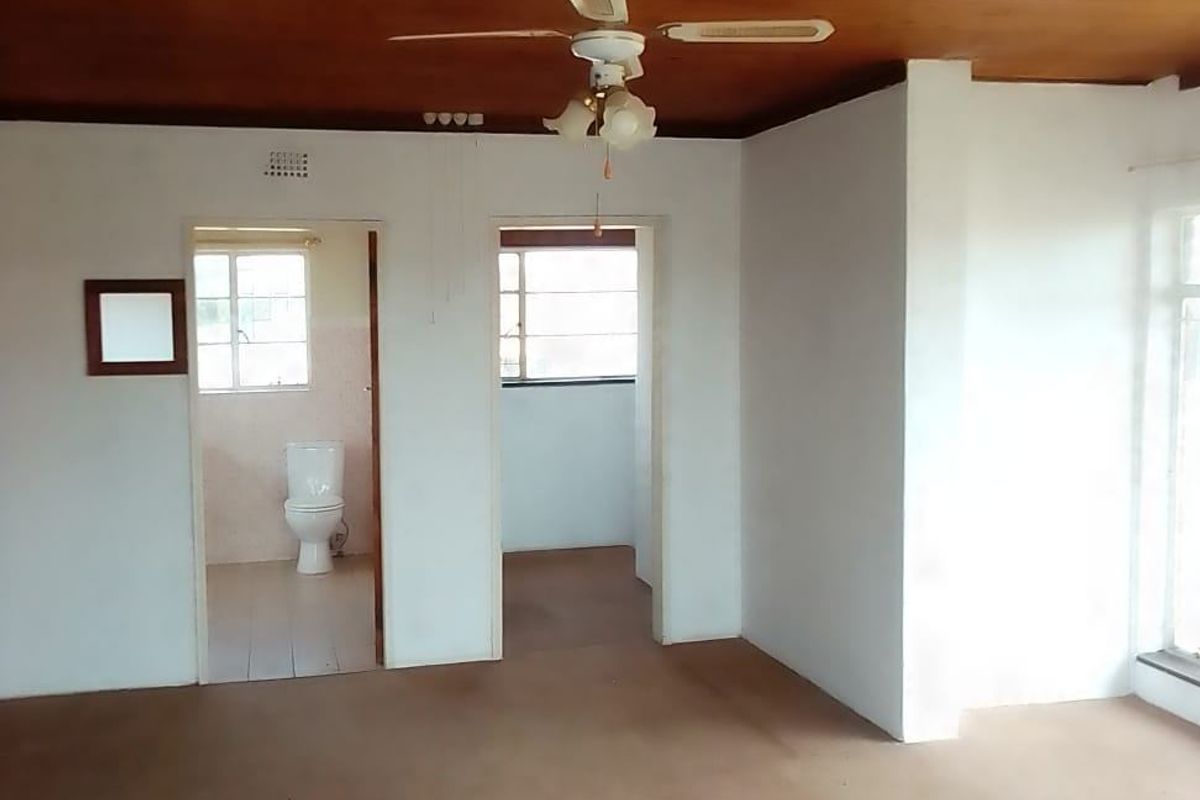 An empty living area featuring a timber ceiling, ceiling fan, and direct access to an adjacent bathroom.