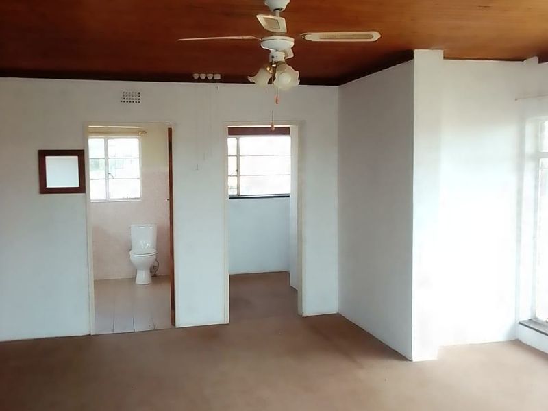 An empty living area featuring a timber ceiling, ceiling fan, and direct access to an adjacent bathroom.