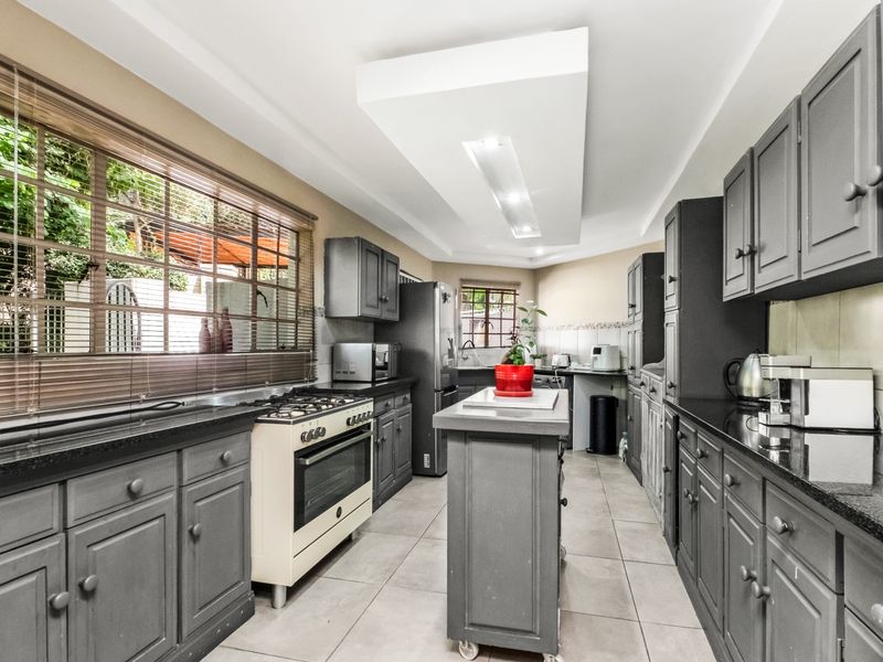 A well-appointed kitchen featuring dark grey cabinetry, granite countertops, a central island, and a gas stove, complemented by tiled flooring and recessed ceiling lighting.