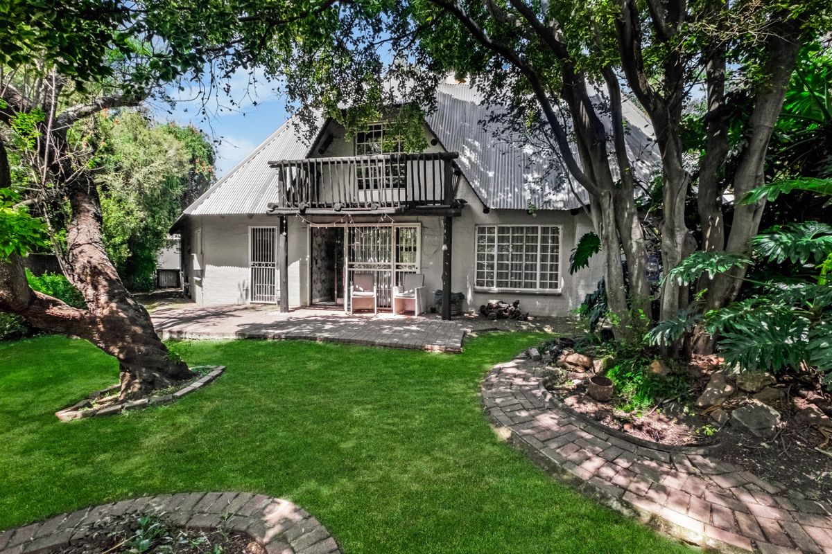Rear view of the house featuring a corrugated metal roof, a wooden balcony, and a brick-paved patio overlooking a lush garden.