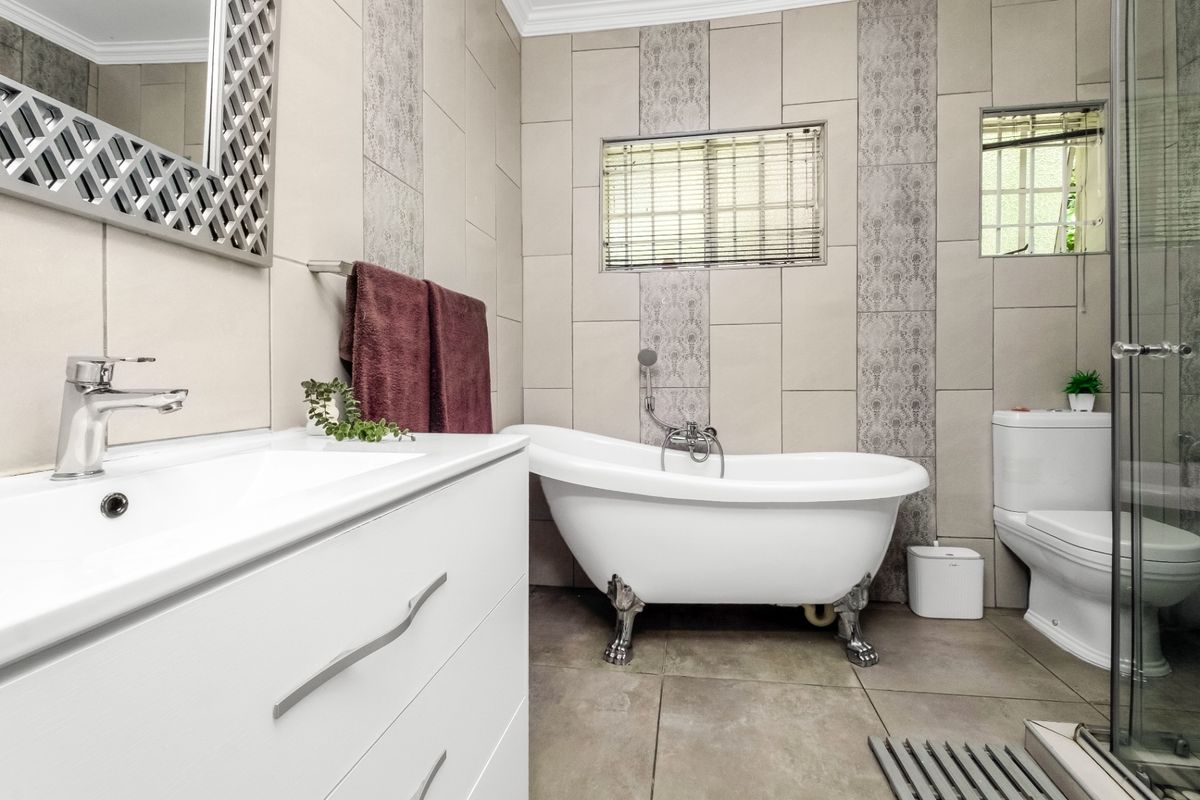 A well-maintained bathroom featuring a classic clawfoot bathtub, modern vanity with basin, toilet, and a separate shower enclosure with neutral tiled finishes.