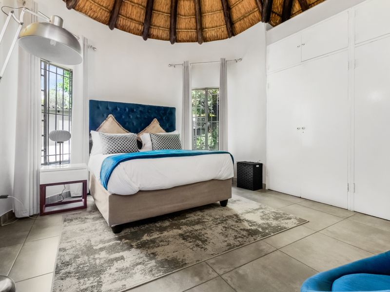 A bright bedroom featuring a unique vaulted thatch ceiling, tiled flooring, and ample built-in cupboard storage.