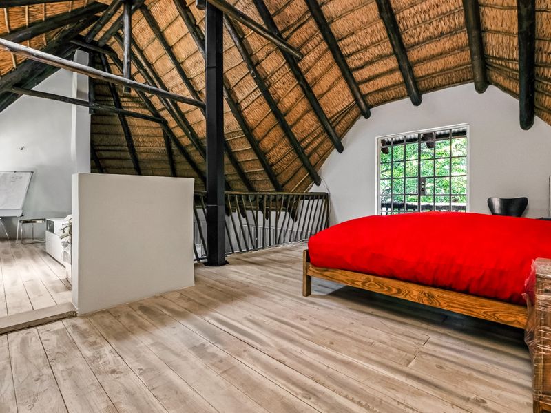 Spacious loft-style bedroom featuring a high vaulted thatched ceiling with exposed timber rafters, timber flooring, and a metal balustrade overlooking the lower level.