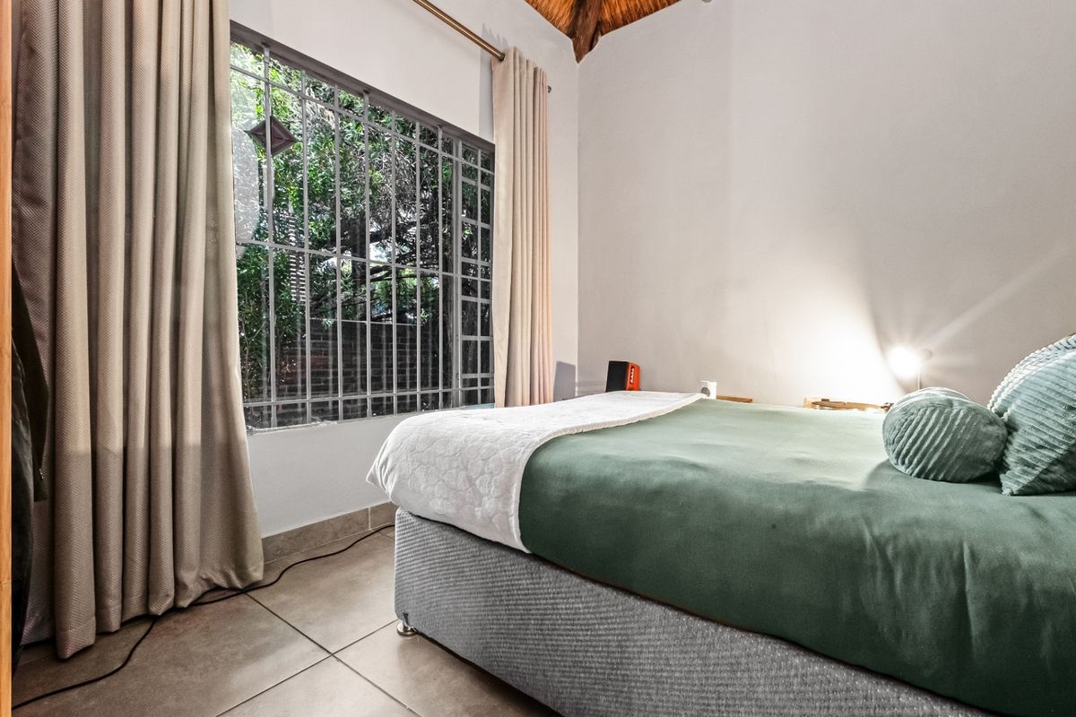 A bedroom featuring tiled flooring, a high thatched ceiling, and a window fitted with security bars.