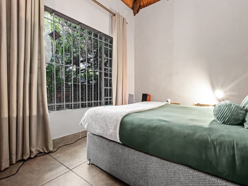 A bedroom featuring tiled flooring, a high thatched ceiling, and a window fitted with security bars.