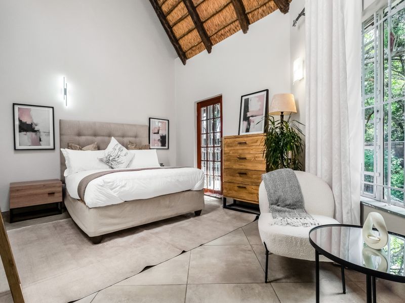 A well-maintained bedroom featuring a high vaulted thatched ceiling with exposed timber rafters, tiled flooring, and direct access to the garden through a glass door.