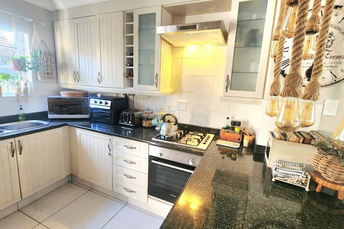 A functional kitchen featuring cream-colored cabinetry, dark granite countertops, a gas hob with an integrated oven, and a double bowl sink.