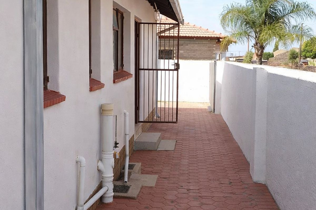 A side exterior walkway featuring paved flooring, a boundary wall, and exposed roof rafters along the side of the house.
