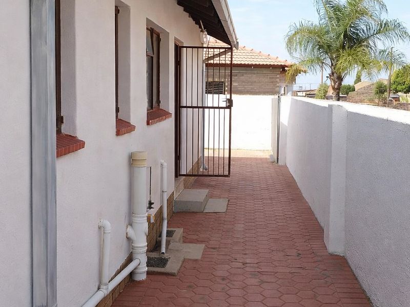 A side exterior walkway featuring paved flooring, a boundary wall, and exposed roof rafters along the side of the house.