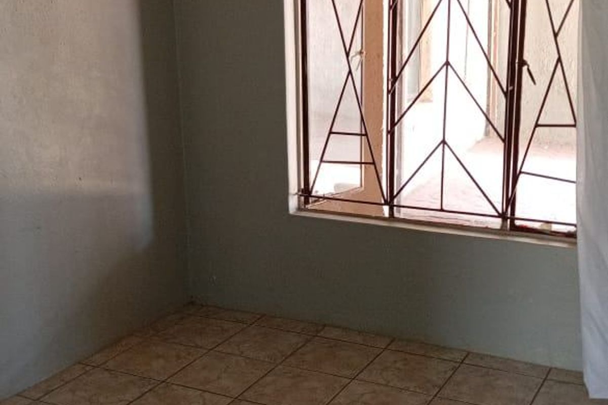 An empty bedroom featuring tiled flooring and security bars on the window, providing a blank canvas for potential interior updates.
