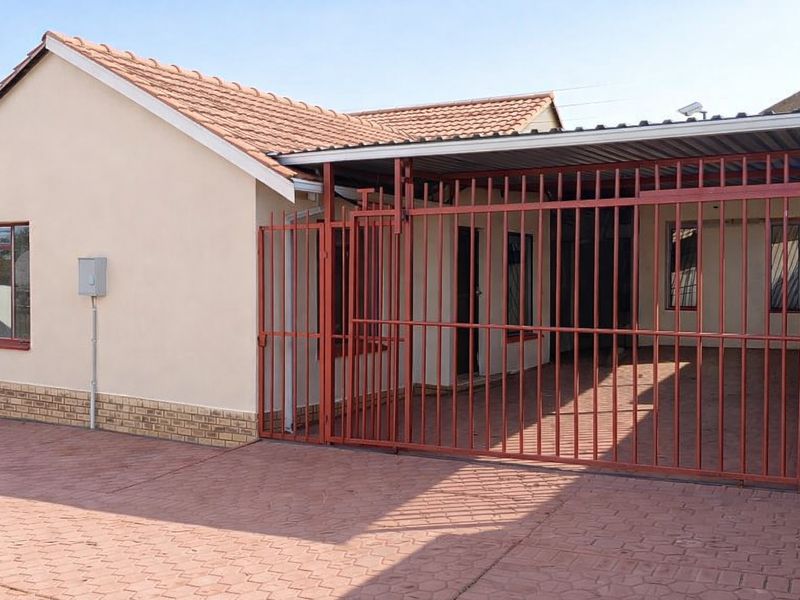 Front exterior view of the house featuring a paved driveway, a secure metal gate, and a covered carport area.