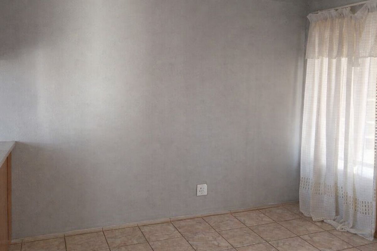 An empty living area featuring neutral grey walls, ceramic floor tiles, and a window with installed curtain tracks.