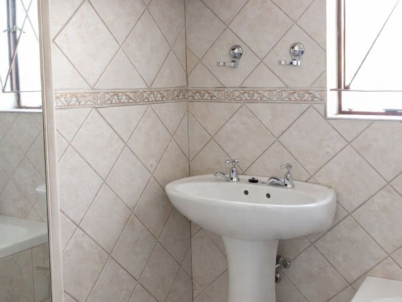 A functional bathroom featuring a pedestal basin, tiled walls with decorative border, and a built-in bathtub.