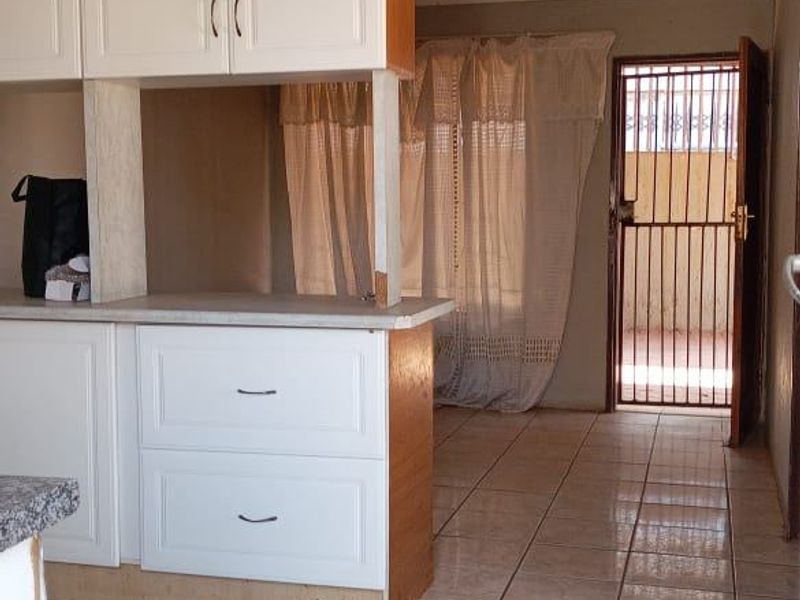 A functional kitchen area featuring built-in cabinetry and tiled flooring, leading directly to an exterior security gate.