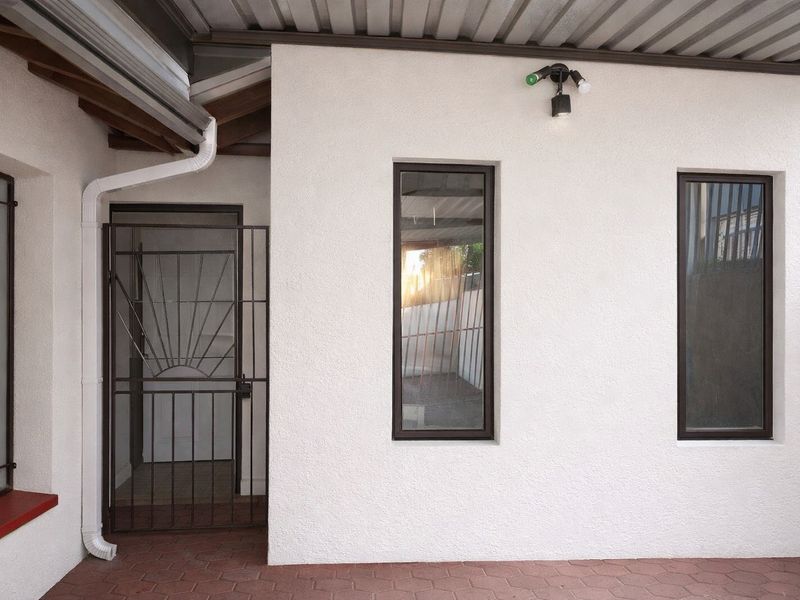 A clean, covered patio area featuring paved flooring, a metal security gate, and modern exterior wall lighting.