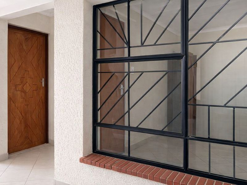 A bright hallway featuring tiled flooring, a textured wall finish, and a secure metal-framed window with a brick sill.
