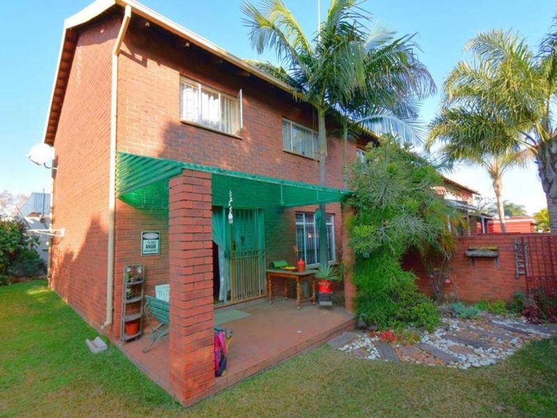 Rear view of the townhouse featuring a red brick facade, a covered patio area with a green roof, and a private garden space.