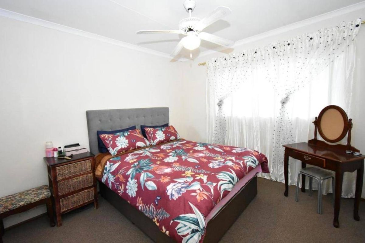 A standard bedroom featuring carpeted flooring, a ceiling fan, and window treatments.