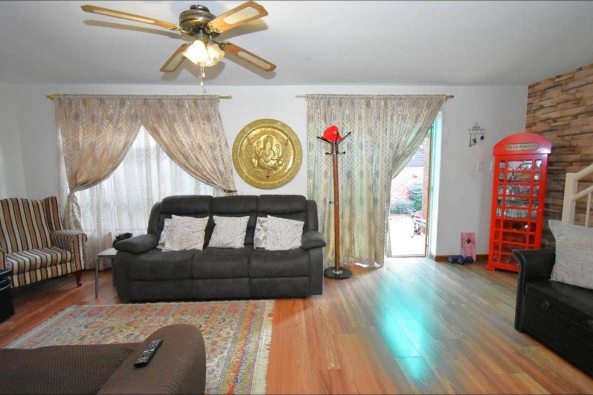 A living room featuring laminate flooring, a ceiling fan, and a stone veneer accent wall with direct access to the exterior.