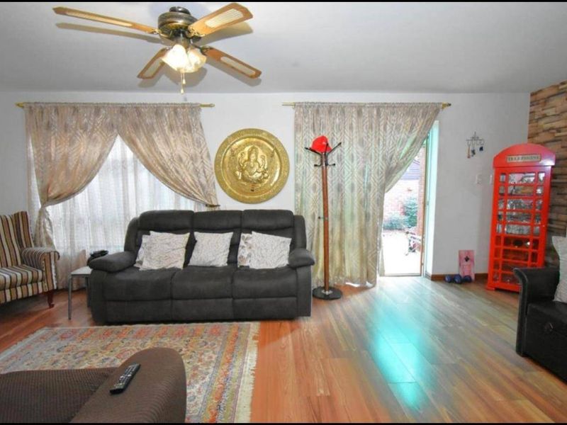 A living room featuring laminate flooring, a ceiling fan, and a stone veneer accent wall with direct access to the exterior.