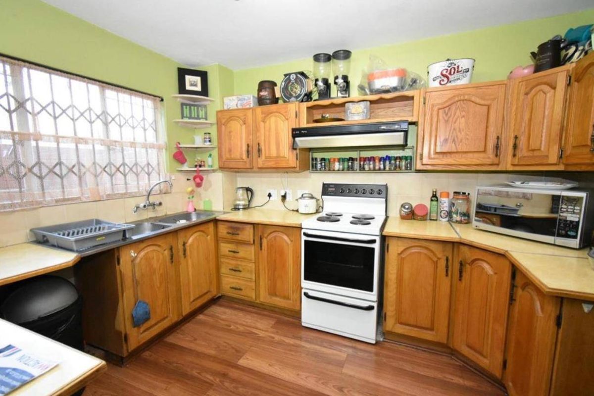 A functional kitchen featuring traditional wooden cabinetry, laminate countertops, a freestanding stove with extractor fan, and a double basin sink with security window bars.