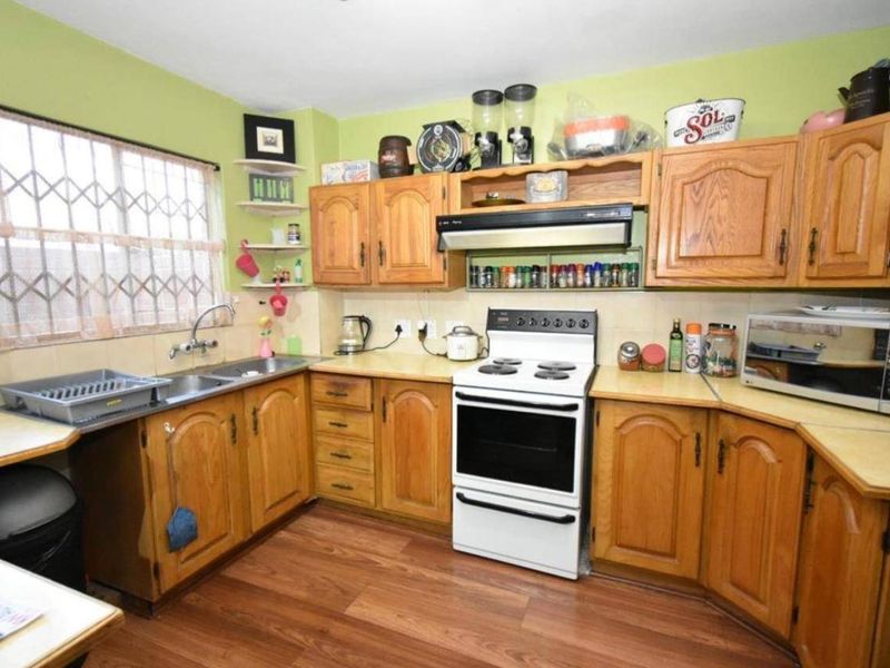 A functional kitchen featuring traditional wooden cabinetry, laminate countertops, a freestanding stove with extractor fan, and a double basin sink with security window bars.