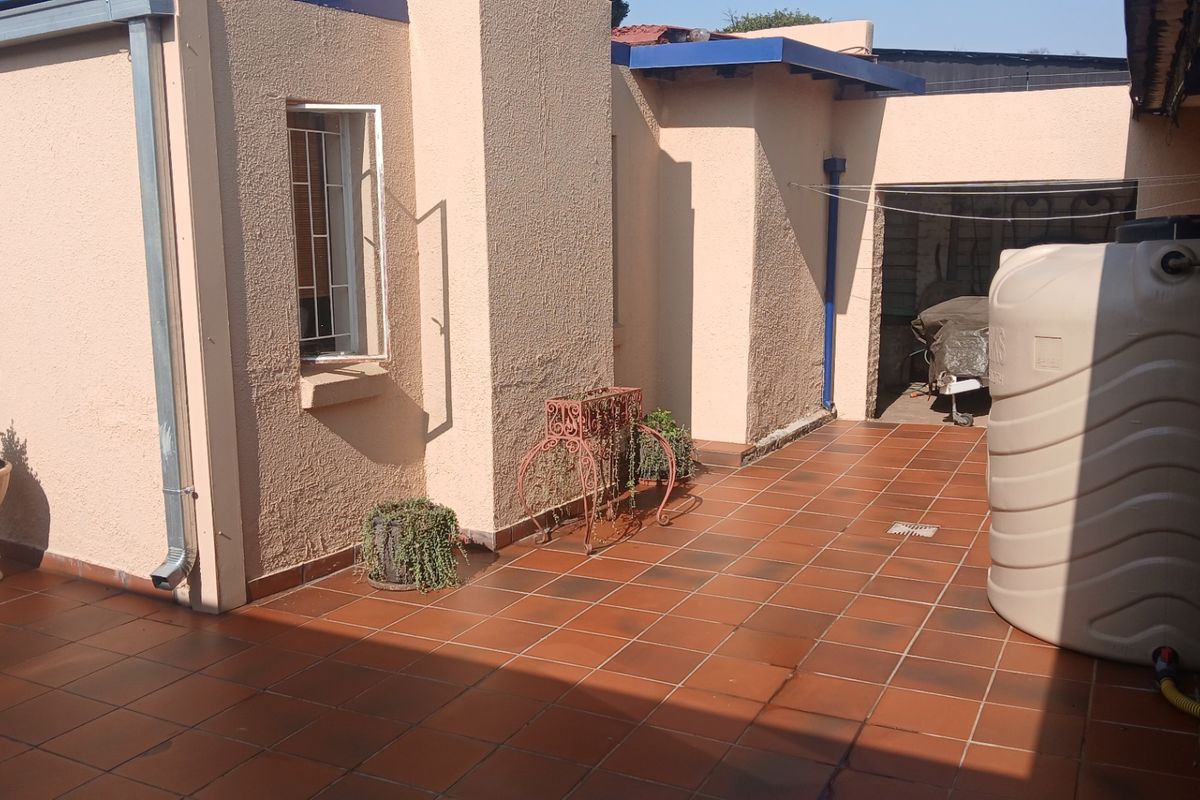 A paved rear patio area featuring a large water storage tank, exterior wall finishes, and drainage infrastructure.