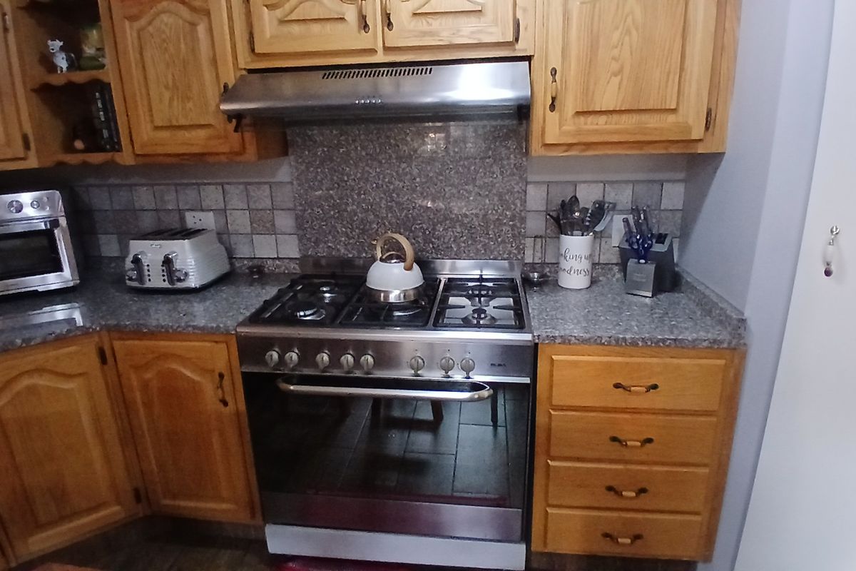 A functional kitchen featuring wooden cabinetry, granite countertops, a tiled backsplash, and a stainless steel gas stove with an integrated extractor fan.