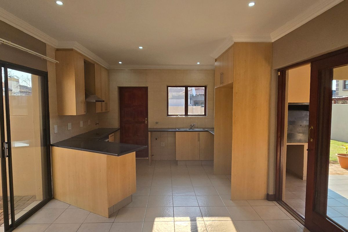 Spacious kitchen featuring light wood cabinetry, stone countertops, and direct access to an outdoor patio area with a built-in braai.