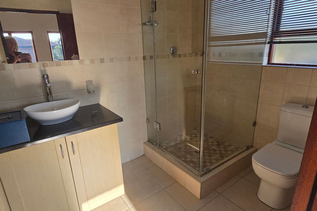 A functional bathroom featuring a vanity with a vessel sink, a glass-enclosed shower, and a toilet, finished with neutral wall and floor tiling.