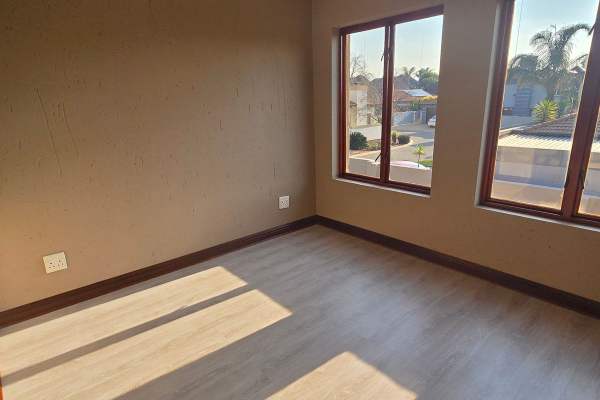 A bright, empty bedroom featuring light-toned laminate flooring, timber-framed windows, and neutral wall finishes, offering a clean canvas for personalization.