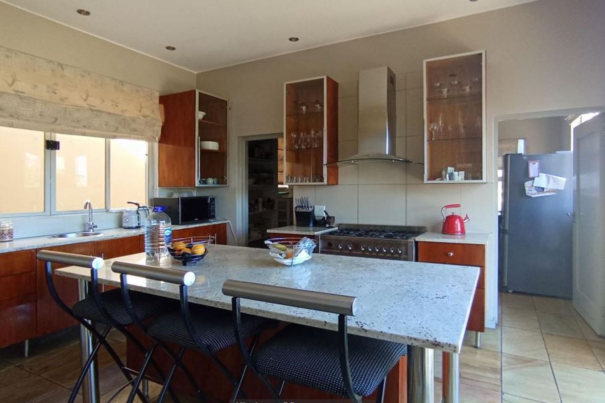 A functional kitchen featuring a granite-topped island, gas hob, stainless steel extractor fan, and ample fitted cabinetry with tiled flooring.