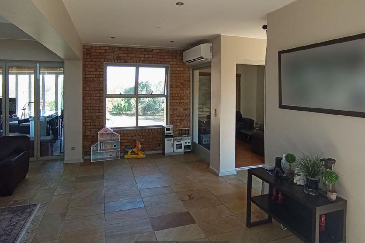 Spacious living area featuring stone tile flooring, an exposed brick feature wall, and integrated split system air conditioning with access to an outdoor patio.