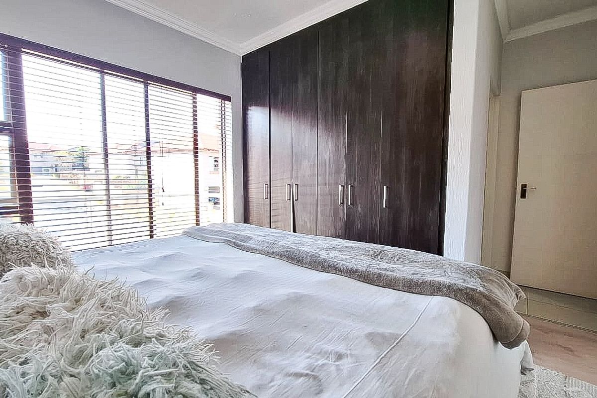 A well-lit bedroom featuring dark wood built-in cupboards, neutral wall finishes, and venetian blinds.