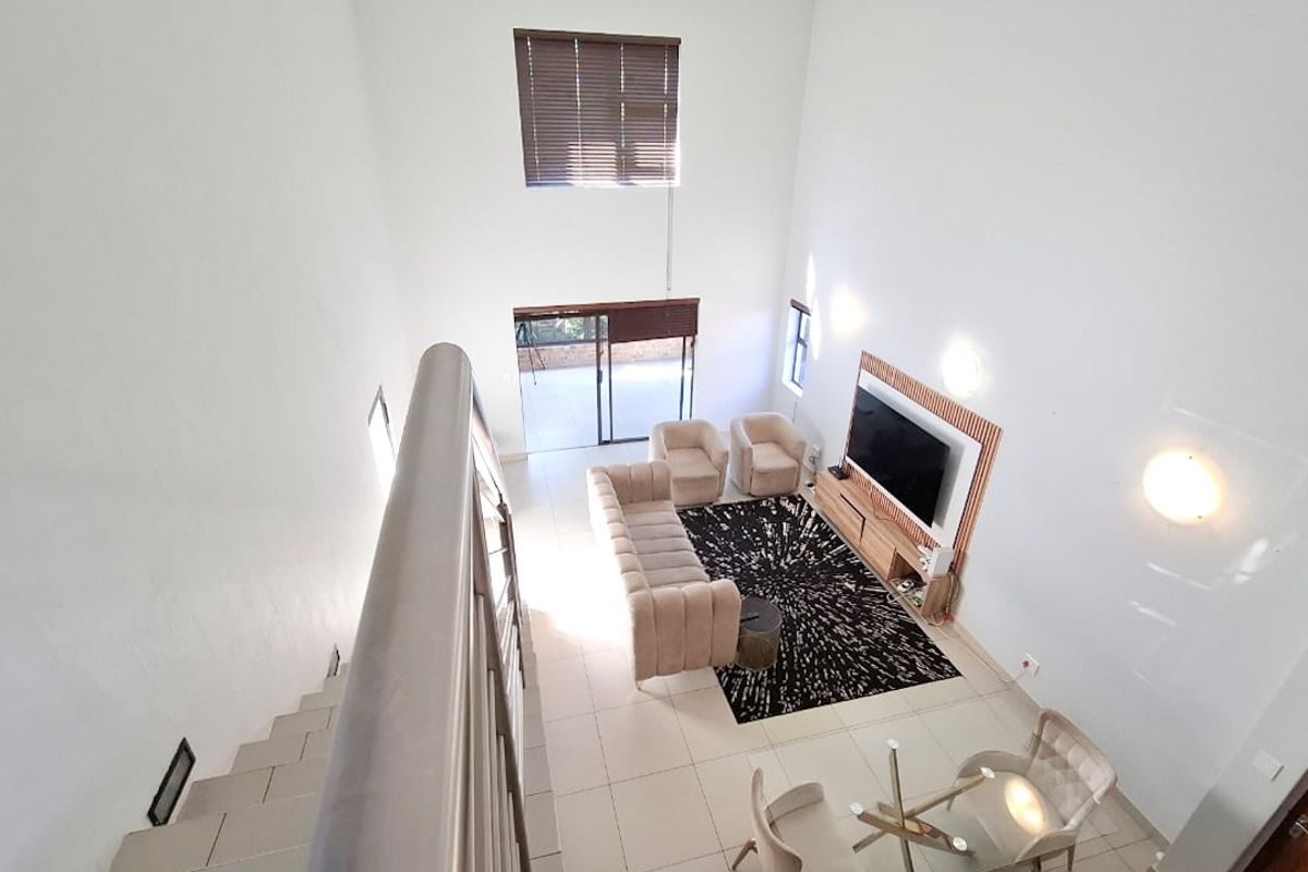 Spacious double-volume living area featuring tiled floors, abundant natural light, and direct access to an outdoor patio through sliding glass doors.