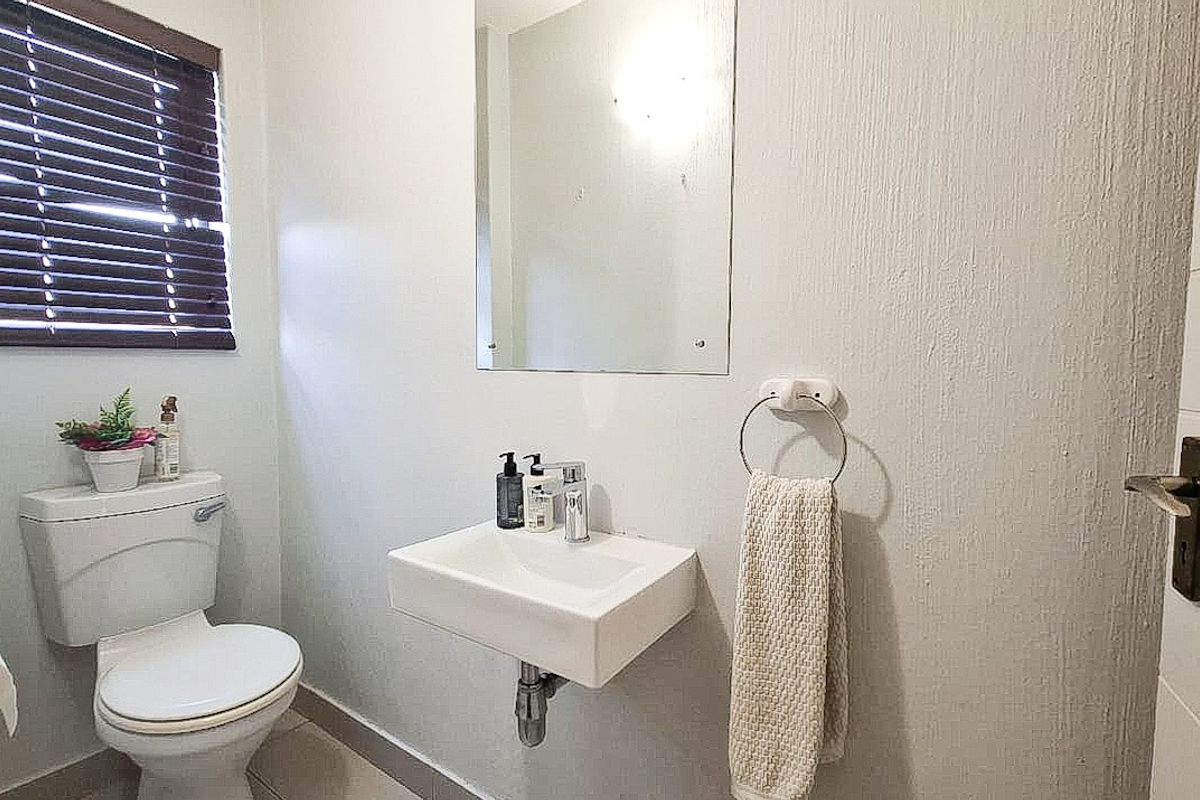 A functional guest bathroom featuring a wall-mounted basin, toilet, and wall mirror with neutral finishes.