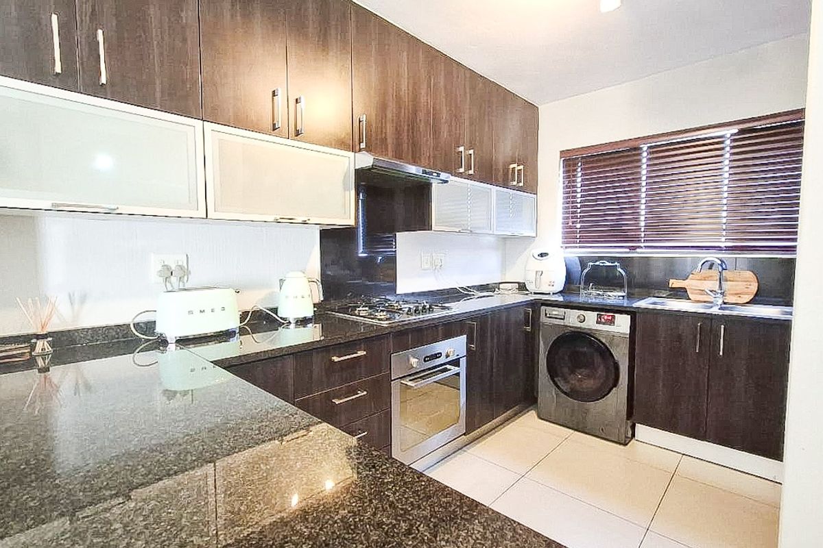 Modern kitchen featuring dark wood cabinetry, granite countertops, built-in oven, gas hob, and integrated laundry appliance space with tiled flooring.
