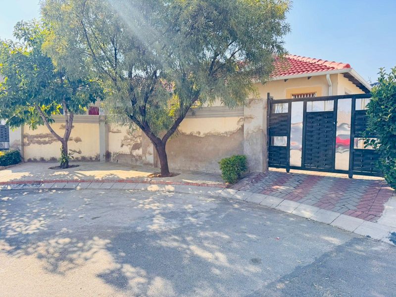 Front view of the property featuring a perimeter wall, metal driveway gate, and paved entrance area with mature trees.