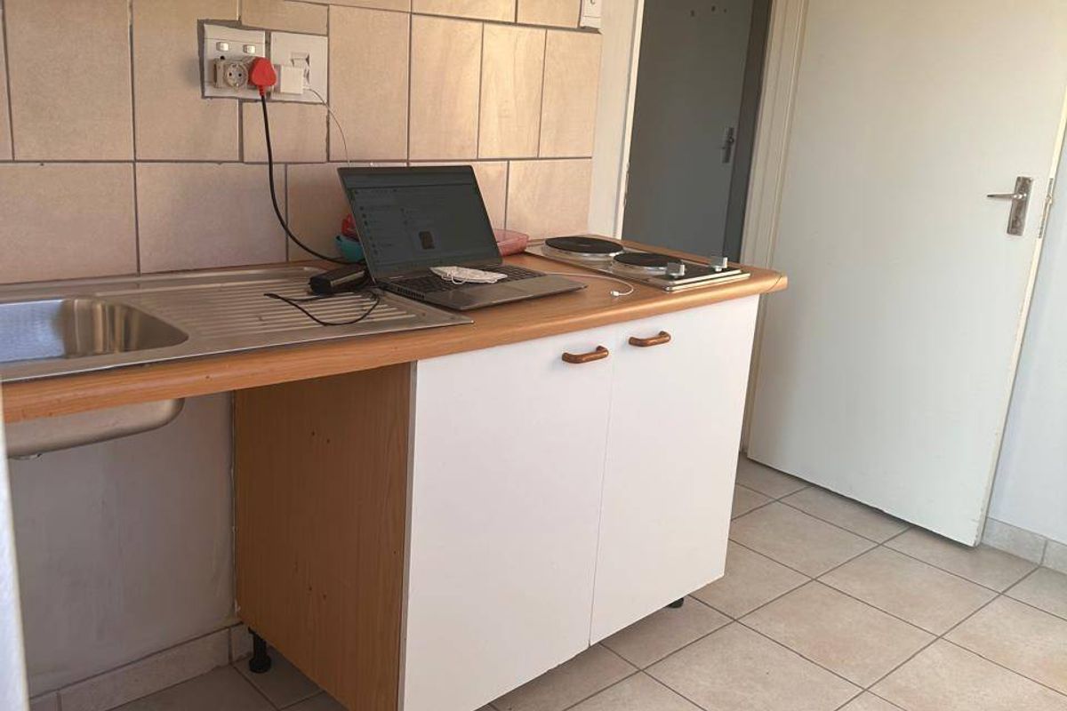 Compact kitchenette featuring a stainless steel sink, built-in hob, tiled splashback, and laminate cabinetry with ceramic floor tiles.