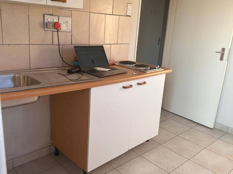 Compact kitchenette featuring a stainless steel sink, built-in hob, tiled splashback, and laminate cabinetry with ceramic floor tiles.