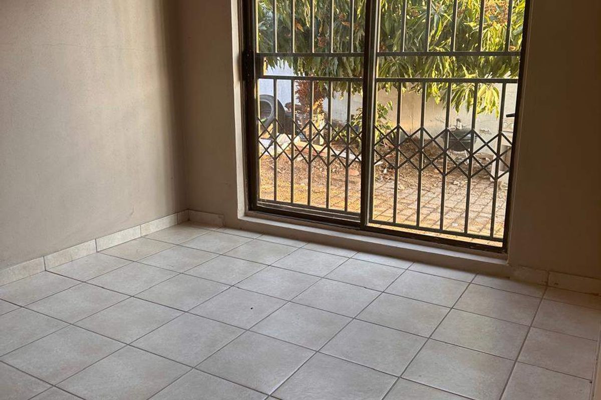 An empty living room featuring neutral ceramic floor tiles and a sliding glass door with a security gate leading to the garden.