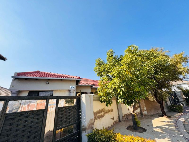 Front exterior view of the property featuring a tiled roof, metal gate, and boundary wall with visible plaster and paint wear.