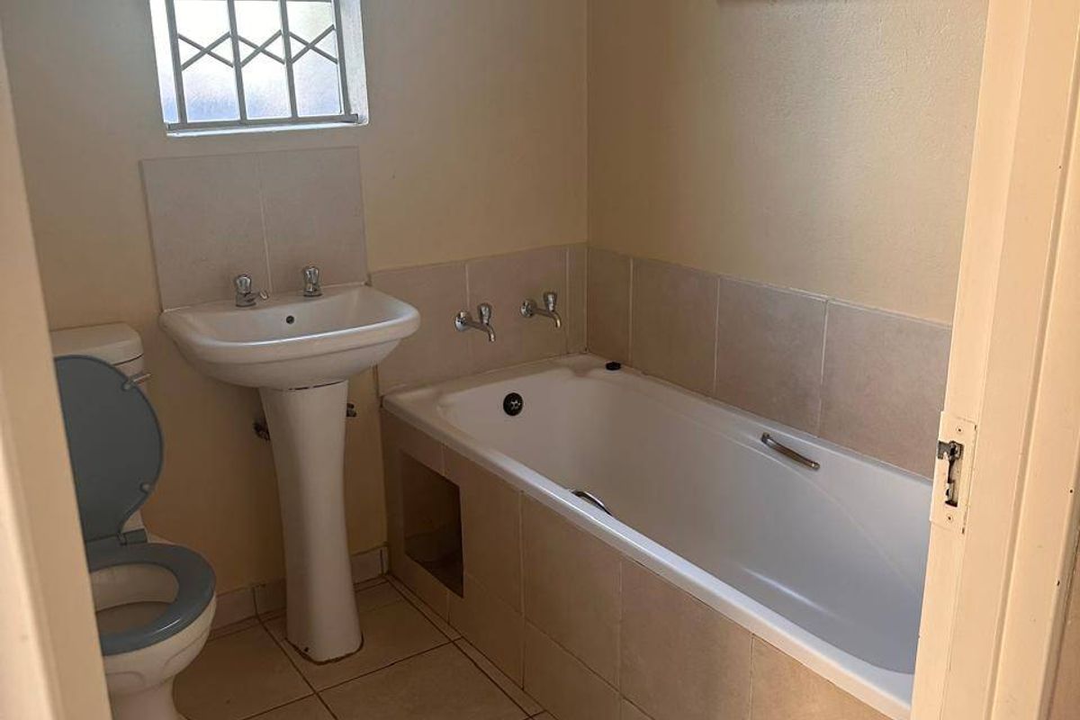 A functional bathroom featuring a pedestal basin, built-in bathtub, and tiled flooring, offering a clean canvas for potential cosmetic updates.
