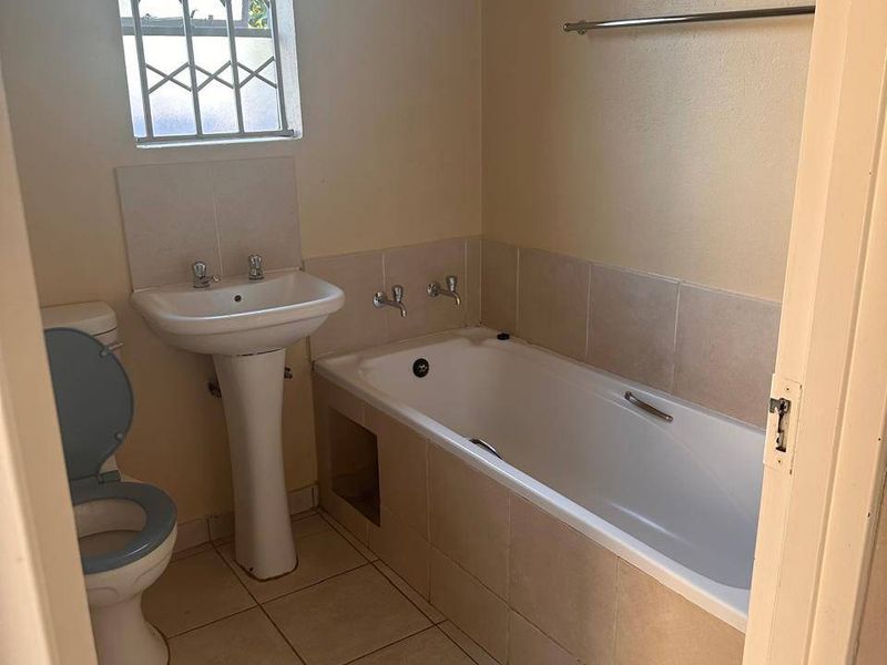 A functional bathroom featuring a pedestal basin, built-in bathtub, and tiled flooring, offering a clean canvas for potential cosmetic updates.