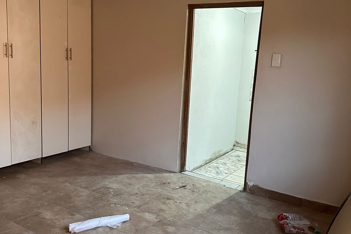 An empty bedroom featuring tiled flooring, built-in cupboards, and decorative ceiling tiles, currently in need of finishing touches and minor repairs.