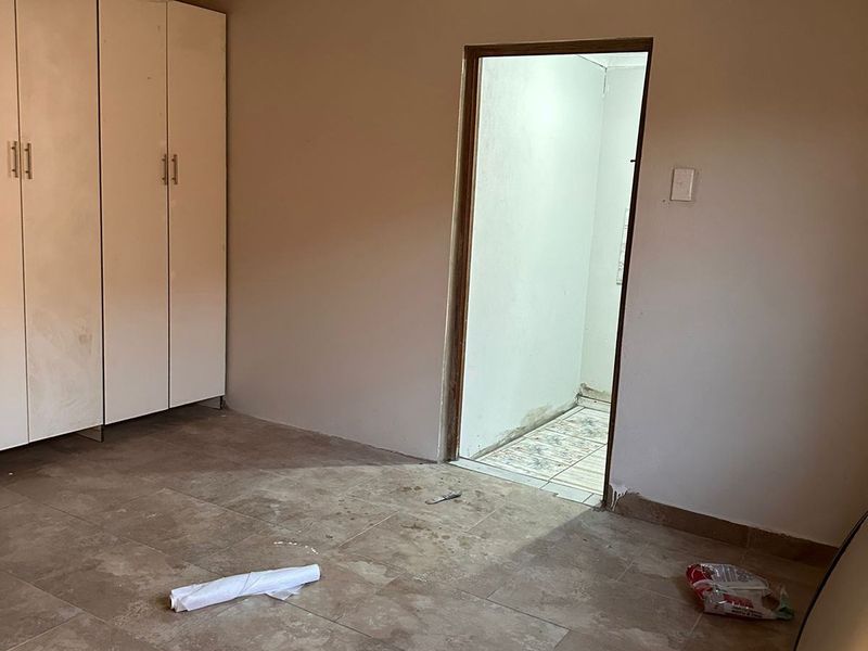 An empty bedroom featuring tiled flooring, built-in cupboards, and decorative ceiling tiles, currently in need of finishing touches and minor repairs.