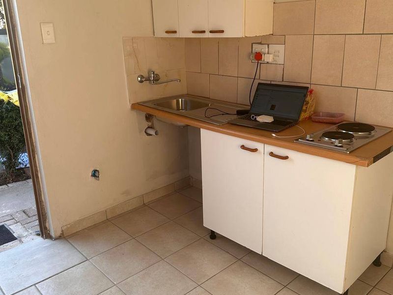 A compact kitchen area featuring basic cabinetry, a stainless steel sink, and an electric hob with tiled splashback and flooring.