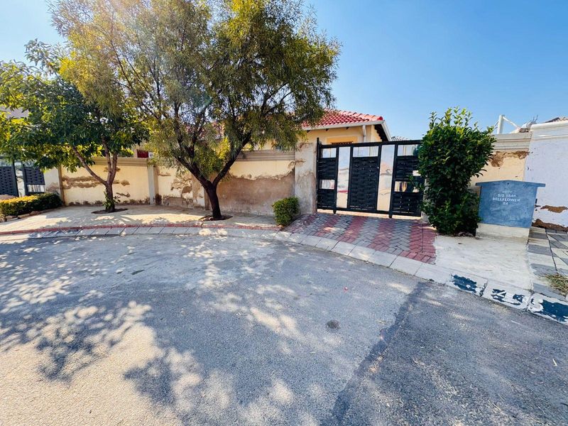 Front exterior view of the property featuring a metal gate, paved driveway, and perimeter wall with visible weathering and plaster damage.