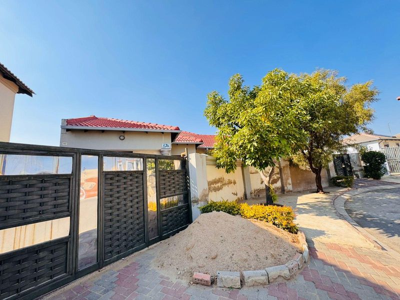 Front exterior view of the property featuring a metal gate, paved driveway, and perimeter wall with visible plaster and paint deterioration.